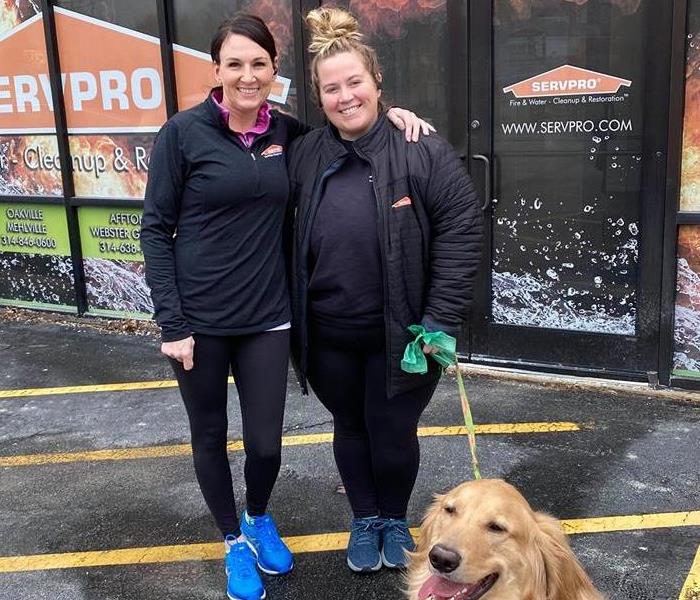 Two people outside of a SERVPRO with a golden retriever. 