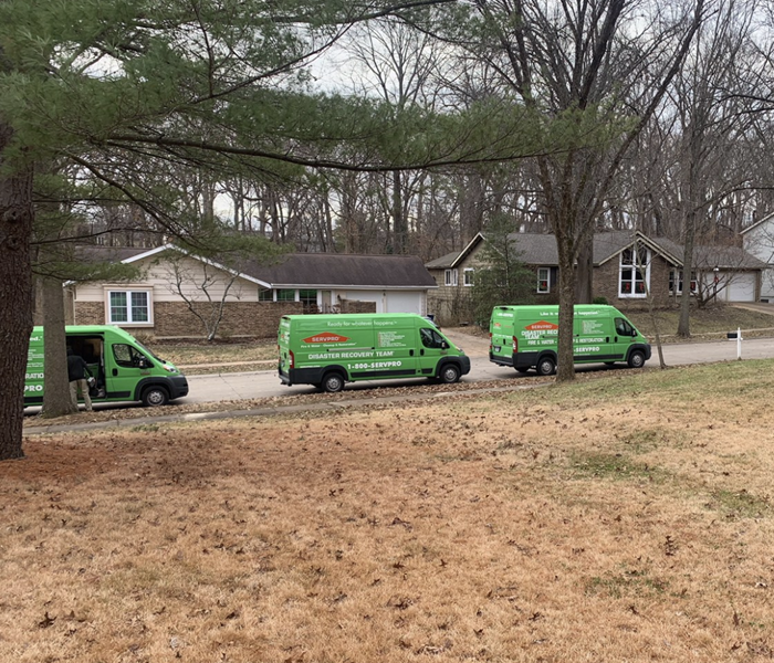 Three green trucks park on the side of a street. 