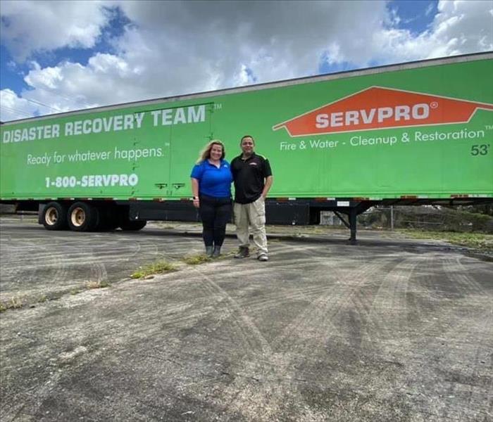 Two people in front of a green SERVPRO trailer.
